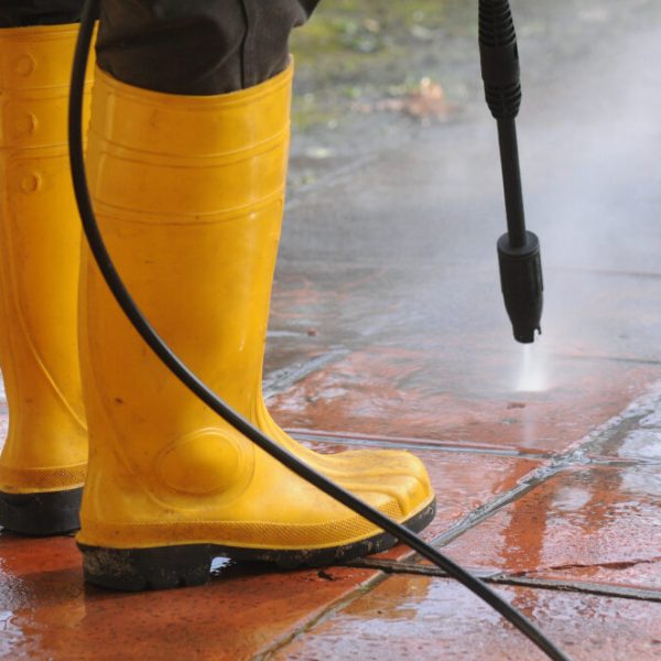 persona-vestida-botas-goma-amarilla-boquilla-agua-alta-presion-limpiando-suciedad-baldosas